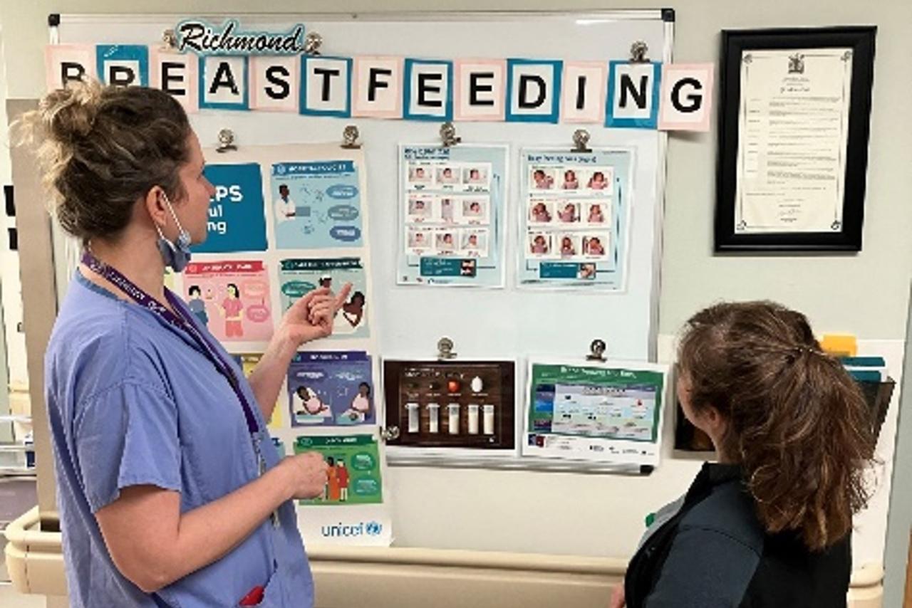 A lactation consultant talking with a patient in front of a poster with breastfeeding resources