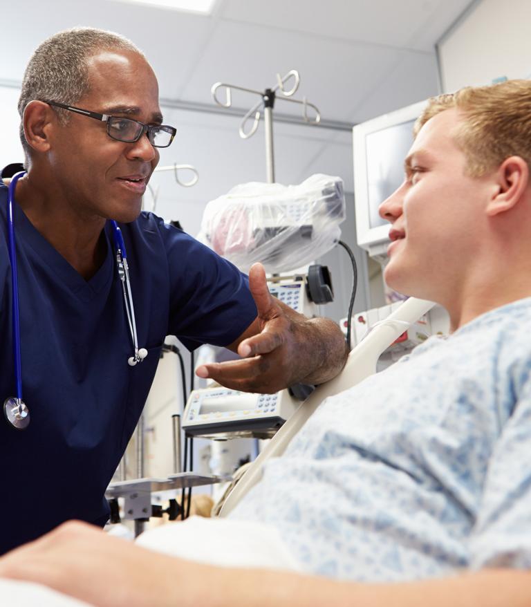 A doctor leaning over providing support to an adult in a hospital bed
