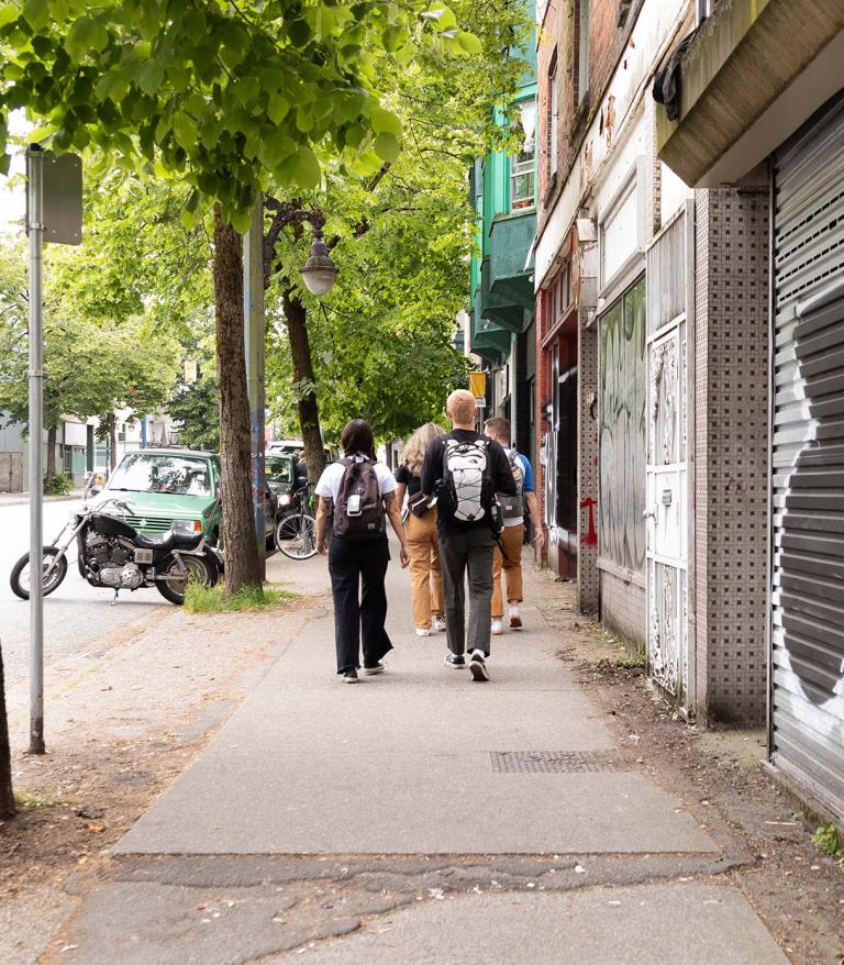 group of four people walking down a tree-lined urban street
