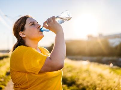 person drinking water on a sunny day after running in a public park