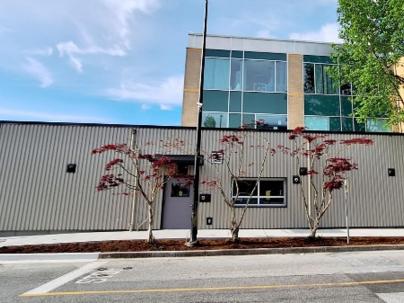 Exterior photo of a building with grey metal siding and trees in front