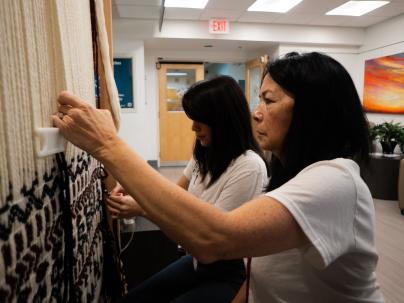 Two women working on weaving an item on the wall