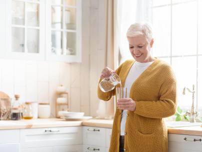 An older woman pouring herself a glass of water in a sunny kitchen