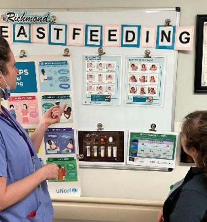 A lactation consultant talking with a patient in front of a poster with breastfeeding resources