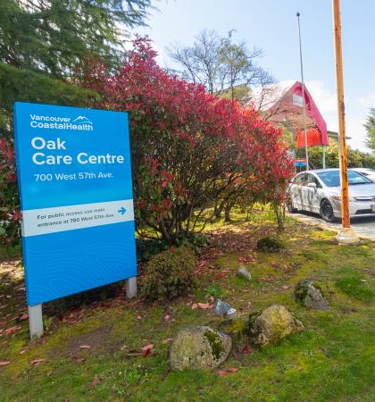 blue sign saying Oak Care Centre in front of bushes and trees with blue sky in the background